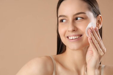 Pamuk yastıklı genç bir kadın kahverengi arka plandaki makyajı temizliyor, yakın plan.