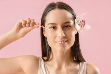 Çiçekli ve pamuklu genç bir kadın pembe arka planda göz makyajını temizliyor, yakın plan.