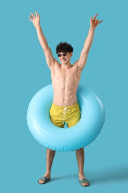 Mavi arka planda şişirilebilir yüzüğü olan yakışıklı genç adam.