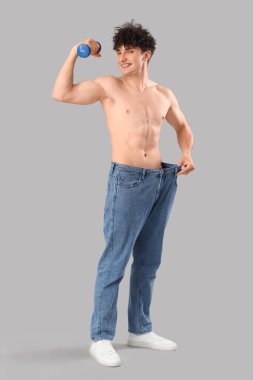 Gri arka planda dambılı bol kotlu yakışıklı, mutlu sporcu. Kilo verme konsepti