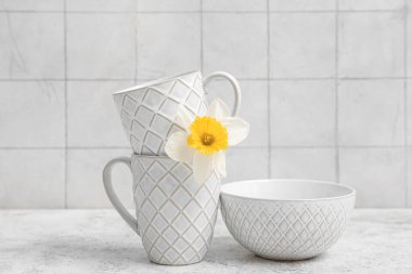 Beyaz fayans duvarının yanındaki grunge masasında nergis çiçeği olan güzel sofra takımı