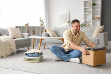 Genç adam evde katlanmış giysileri kutuya koyuyor.