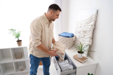 Genç adam katlanmış giysileri evdeki çekmeceye koyuyor.