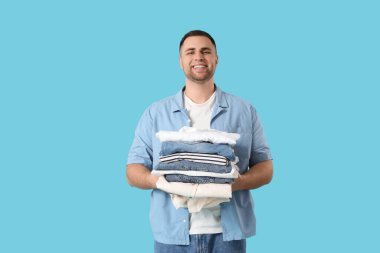 Mavi arka planda bir yığın elbisesi olan genç adam.