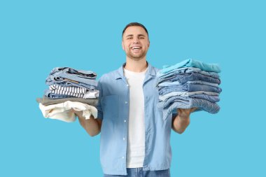 Mavi arka planda bir yığın elbisesi olan genç adam.