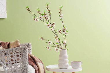 Çiçek açan dalları ve yeşil duvarın yanındaki sehpanın üzerinde çay fincanı olan vazo, yakın plan.