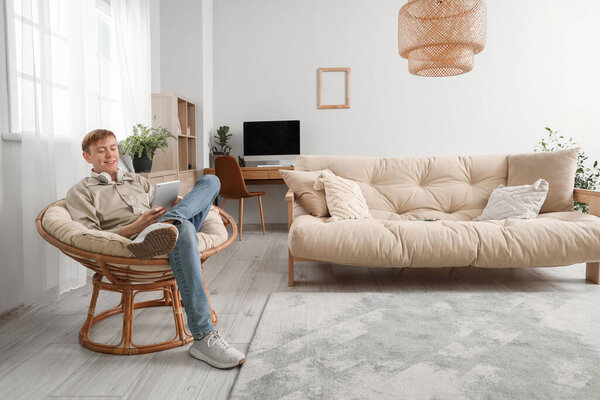 Молодой человек в наушниках с помощью планшетного компьютера в кресле дома