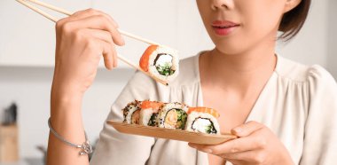 Genç Asyalı kadın mutfakta lezzetli suşi yiyor, yakın plan.