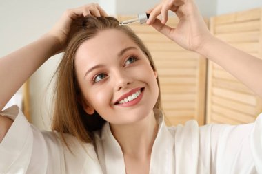 Evde saç dökülmesi tedavisi için serum kullanan genç bir kadın.