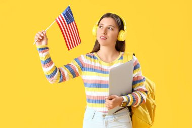 Sarı arka planda ABD bayrağı ve dizüstü bilgisayarı olan kız öğrenci.