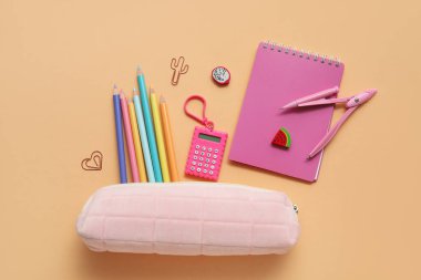 Farklı okul kırtasiyesine ve kahverengi arka planda not defterine sahip pembe kalem kutusu.