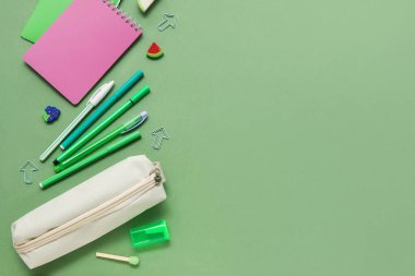 Farklı okul kağıtları ve yeşil arkaplan üzerine not defterleri olan bej renkli kalem çantası.