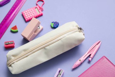 Farklı okul kırtasiyesi ve mor arka planda not defteri olan bej renkli kalem çantası.