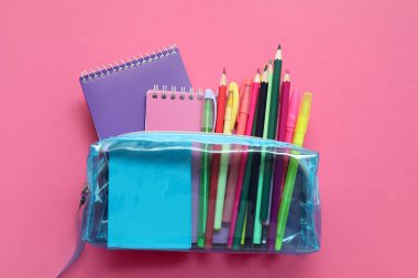 Farklı okul kırtasiyesine ve pembe arkaplan üzerine not defterlerine sahip mavi kalem çantası.