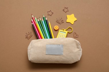 Kahverengi arka planda farklı okul kırtasiyesine sahip bej kalem kutusu.