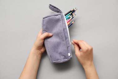 Kalem kutulu çocuk elleri ve gri arka planda renkli kalemler.