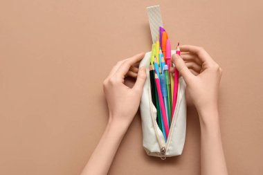 Kalem kutulu çocuk elleri ve kahverengi arka planda farklı okul kağıtları.