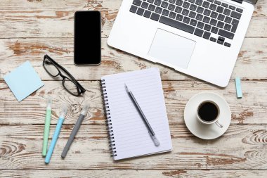 Laptop, bir fincan kahve ve bej ahşap masada kırtasiye malzemesi.
