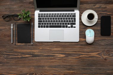 Laptop, bir fincan kahve ve ahşap masada kırtasiye malzemesi.