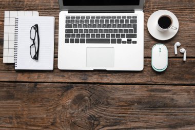 Laptop, bir fincan kahve ve ahşap masada kırtasiye malzemesi.