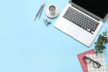 Laptop, bir fincan kahve ve mavi arka planda kırtasiye malzemesi.