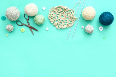 Turkuaz arka planda örgü iğneleri, iplik topları ve makas.