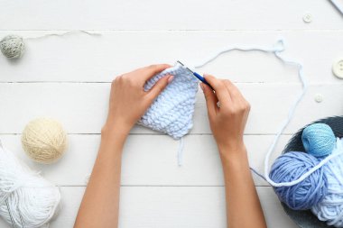 Beyaz ahşap arka planda iplik toplarıyla örgü ören kadın
