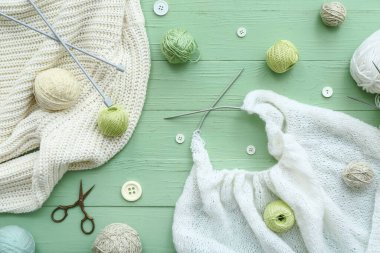 Yeşil ahşap arka planda örülmüş süveter, iğneler ve iplik topları