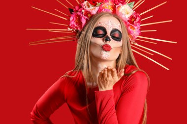 Yüzünde boyalı kafatası olan genç bir kadın kırmızı arka plana öpücük yolluyor. Meksika Ölüler Günü 'nün Kutlaması (El Dia de Muertos)