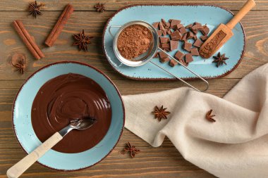 Bir kase lezzetli eritilmiş çikolata ve tahta arka planda kakao tozu.