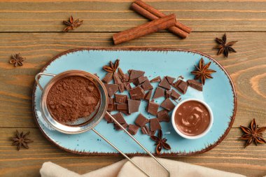 Bir kase lezzetli eritilmiş çikolata ve tahta arka planda kakao tozu.