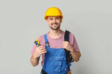 Erkek elektrikçinin portresi. Gri arka planda tel ve tutacağı var.