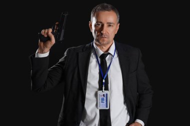Siyah arka planda silahı olan olgun bir FBI ajanı.