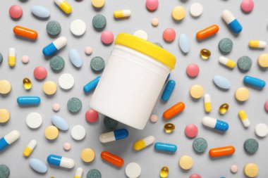 Gri arka planda şişe ve farklı renkli haplar.