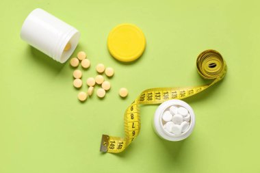 Kilo verme hapları ve yeşil arka planda şerit bulunan şişeler.