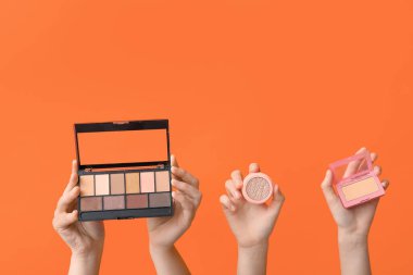 Göz farı paleti ve turuncu arka planda pudra olan kadın elleri