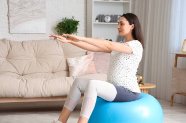 Güzel, genç, hamile bir kadın evde fitbol antrenmanı yapıyor.