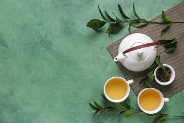 Yeşil arkaplanda yaprakları olan çaydanlık ve fincanlar