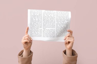 Pembe arka planda gazetesi olan kadın eller.