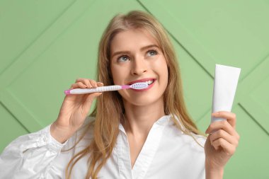 Dişlerini fırçalayan ve yeşil arka planda diş macunu tüpü tutan genç bir kadın.