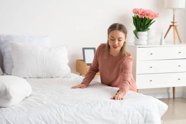 Güzel genç bir kadın hafif yatak odasında yatağını yapıyor.