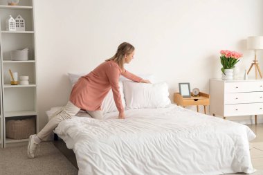 Güzel genç bir kadın hafif yatak odasında yastığı yatağa koyuyor.