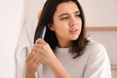 Stressed young woman combing hair in light bathroom clipart