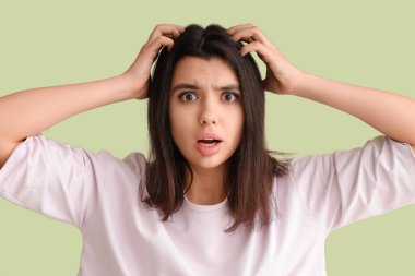 Young woman with dandruff problem scratching head on green background clipart