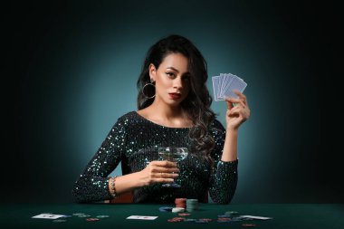Poker masasında oturan genç ve güzel Afro-Amerikalı kadın. Koyu yeşil arka planda iskambil kağıtları, cipsler ve bir bardak şampanyayla.