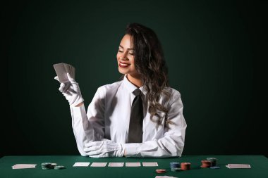 Poker masasında oturan güzel Afro-Amerikalı kadın. Koyu yeşil arka planda kart ve çiplerle oynuyor.