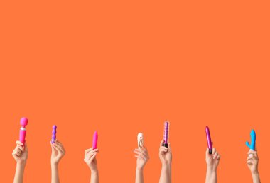 Turuncu arka planda farklı vibratörlere sahip kadın elleri.