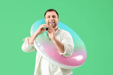 Yeşil arka planda şişme yüzük ve dürbünü olan genç bir adam.