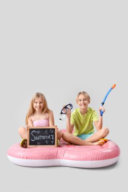 Küçük şirin çocuklar ellerinde yazı tahtası ve şnorkelle dalış teçhizatı tutarken şişme yatakta gri arka planda oturuyorlar.