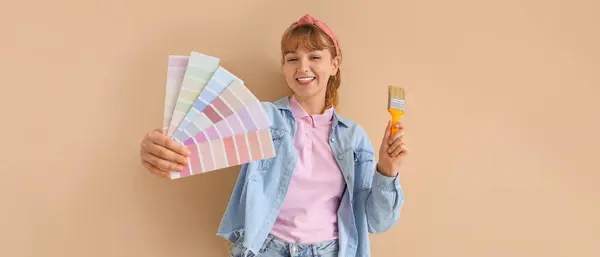 Happy woman with paint color samples and brush on beige background